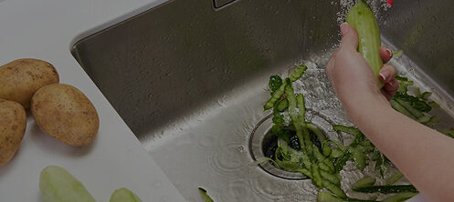 Person washing vegetables in a sink with a garbage disposal