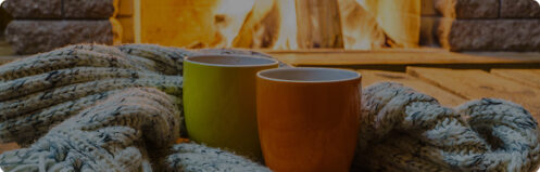 Coffee mugs on a cozy blanket in front of a wood fireplace