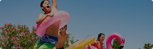 Children jumping into pool in the summer with colorful pool floaties