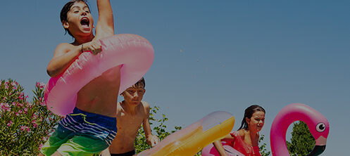 Children jumping into pool in the summer with colorful pool floaties
