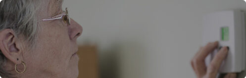 Elderly woman adjusting temperature on her thermostat