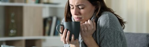 Woman getting cold holding coffee mug at home